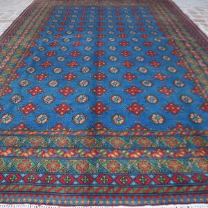 Puede incluir: Una alfombra azul y roja con un dise&ntilde;o geom&eacute;trico. La alfombra tiene un borde de flecos.