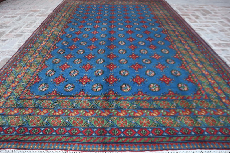 Puede incluir: Una alfombra azul y roja con un dise&ntilde;o geom&eacute;trico. La alfombra tiene un borde de flecos.