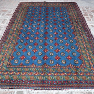 Puede incluir: Una alfombra azul con un patr&oacute;n repetitivo de formas geom&eacute;tricas rojas y blancas. La alfombra tiene un borde con un dise&ntilde;o floral en tonos de verde, rojo y naranja.