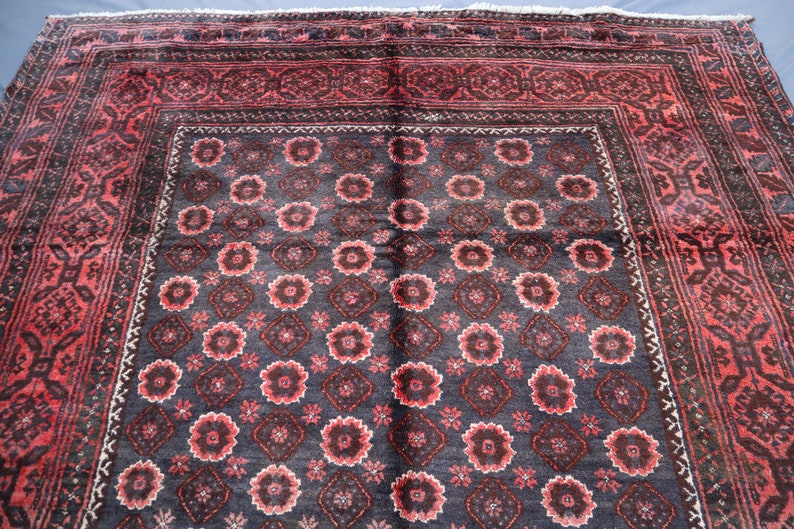 May include: A vintage Persian rug with a dark blue background and a repeating pattern of red and white flowers. The rug has a red border with intricate designs.