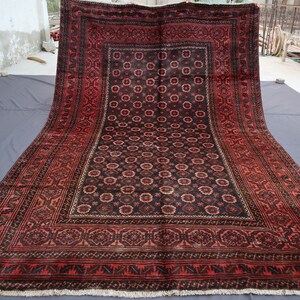 May include: A large, red and black rug with a intricate floral pattern. The rug has a border with a geometric design.