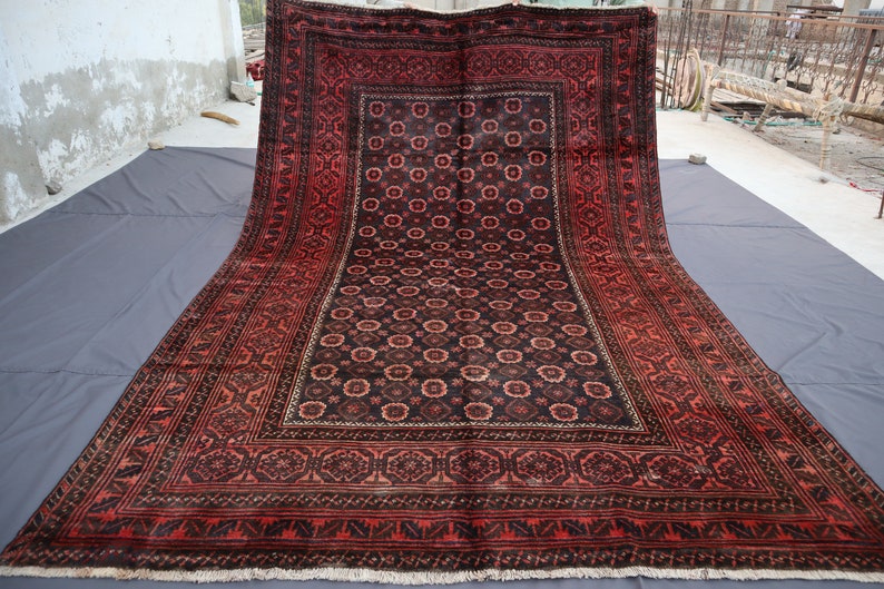 May include: A large, red and black rug with a intricate floral pattern. The rug has a border with a geometric design.