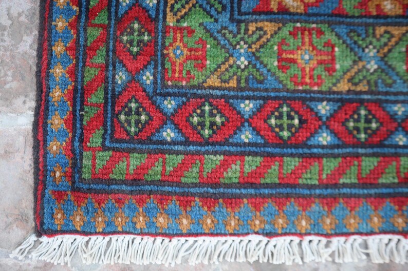 Puede incluir: Primer plano de una alfombra colorida con un patr&oacute;n geom&eacute;trico. La alfombra tiene un borde de flecos y est&aacute; hecha de lana tejida.
