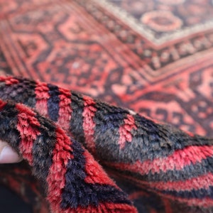 May include: Close-up of a red and black patterned rug with a hand holding the edge of the rug. The rug has a soft, fuzzy texture.