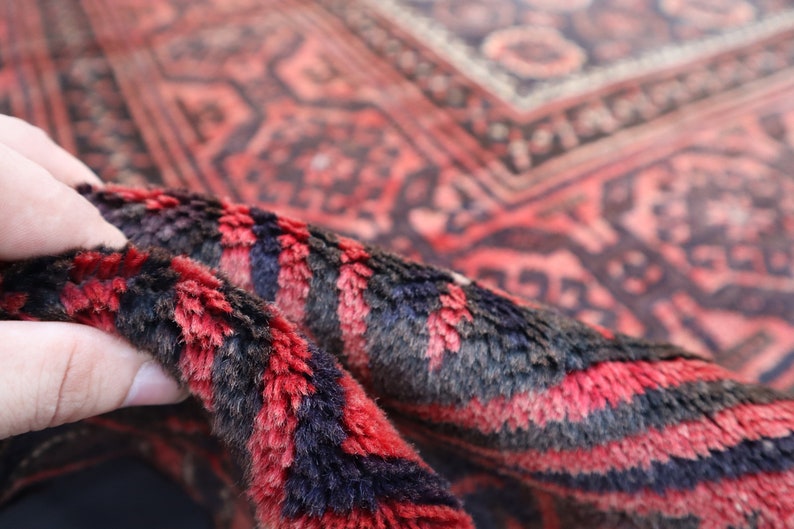 May include: Close-up of a red and black patterned rug with a hand holding the edge of the rug. The rug has a soft, fuzzy texture.