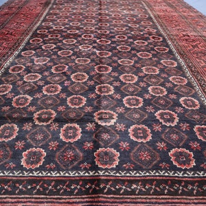 May include: A vintage Persian rug with a dark blue background and a repeating pattern of red and white floral motifs. The rug has a red border with intricate designs.