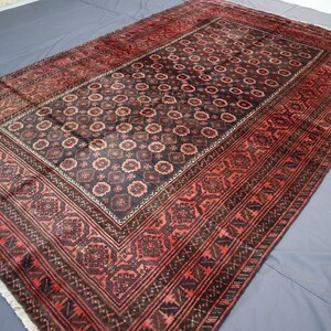 May include: A traditional Persian rug with a dark red and black color scheme. The rug features a central medallion with intricate floral patterns and a border with geometric designs.