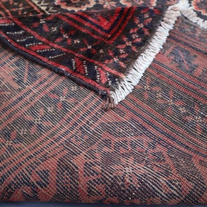 May include: Close-up of a red and blue patterned rug with a fringe border. The rug is folded in half, showing the underside of the fabric.