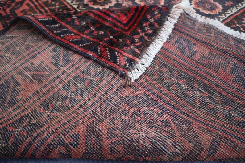 May include: Close-up of a red and blue patterned rug with a fringe border. The rug is folded in half, showing the underside of the fabric.
