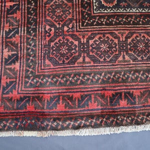 May include: Close-up of a red and black rug with intricate geometric patterns. The rug has a fringe border and is made of wool.