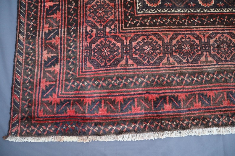 May include: Close-up of a red and black rug with intricate geometric patterns. The rug has a fringe border and is made of wool.