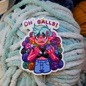 Puede incluir: Una colorida pegatina con un personaje de dibujos animados con pelo turquesa y piel rosa, sosteniendo un ganchillo e hilo. La pegatina tiene el texto "OH BALLS!" y está colocada sobre un fondo de hilo azul y naranja.