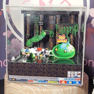 以下が含まれることがあります： 「107 MISS」という文字が書かれた緑色のスライムモンスターが特徴的な、ビデオゲームのシーンを表現した3Dジオラマです。ジオラマは、木々や蔦、はしごのある森の中に設置されています。ゲームのキャラクターの小さなフィギュアも含まれています。