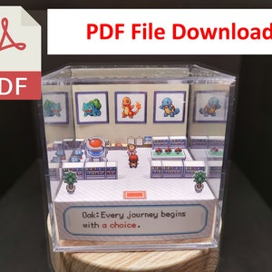 May include: A clear plastic cube diorama of the Pokemon video game. The diorama features a scene from the game with a character standing in front of a building with a sign that reads "Oak: Every journey begins with a choice."