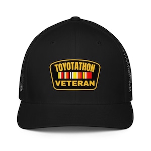 May include: Black baseball cap with a mesh back and a curved brim. The front features a patch with the text "TOYOTATHON VETERAN" in yellow, red, and white. The cap is a classic style, suitable for outdoor activities.