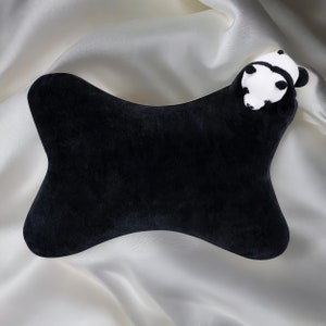 May include: A black plush travel pillow shaped like a bone with a white panda face on one end.