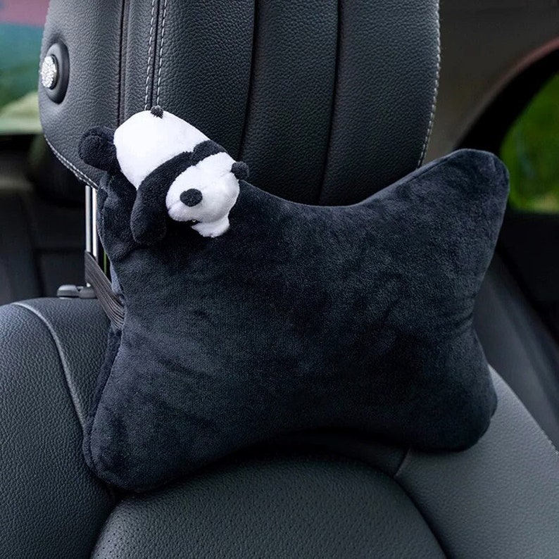 May include: Black car headrest with a plush black and white panda head attached. The headrest is shaped like a pillow and is designed to provide support for the head and neck.