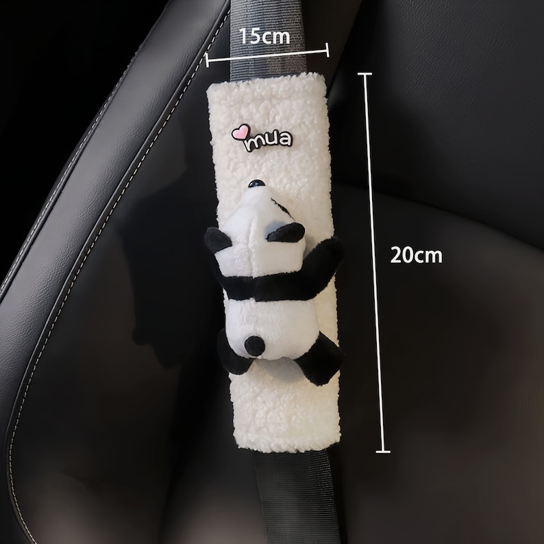 May include: White plush car seatbelt cover with a black and white panda plush toy attached. The cover has a pink heart and the word "mua" embroidered on it. The cover measures 15 inches long and 20 inches wide.