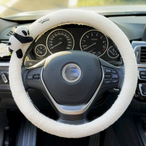 May include: White fluffy steering wheel cover with a panda bear charm attached. The cover has the word "vaiva" printed on it.
