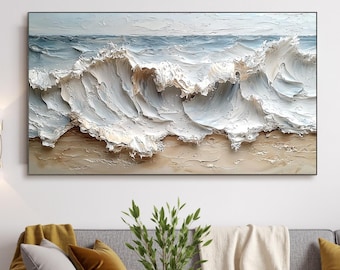 May include: A living room interior design featuring a large abstract painting of white waves crashing on a sandy beach. The painting is hanging on a white wall above a gray sofa with white and yellow throw pillows. A small green plant is in a gold vase on a black coffee table.