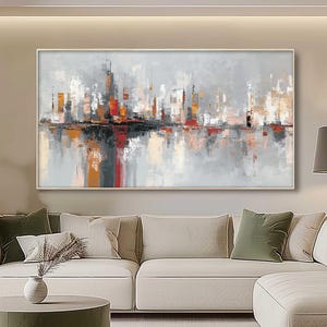 May include: Abstract cityscape painting in a neutral palette. The artwork depicts a skyline with buildings in grey, orange, and red, reflected in water. The framed painting hangs above a modern sofa, creating a contemporary living space.