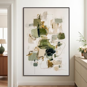 Puede incluir: Impresión artística abstracta con formas verdes, doradas y beige sobre fondo blanco. La obra está enmarcada en un borde negro y cuelga de una pared blanca. La pintura tiene un estilo moderno y minimalista.