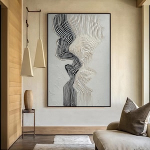 May include: Abstract black and white textured artwork in a black frame. The painting features a flowing design with vertical lines, creating a sense of movement. The artwork is displayed in a modern living space with neutral tones.