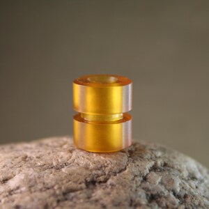 May include: A close-up of a double-layered amber-colored bottle stopper. The stopper is made of a smooth, translucent material and has a slightly rounded shape.