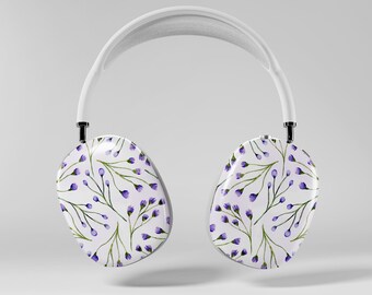 May include: White over-ear headphones with a floral pattern. The earcups feature a white background with a repeating pattern of purple flowers and green stems. The headband is white.