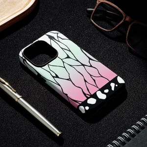 May include: A phone case with a gradient design of light green to pink, featuring black vein-like patterns. The bottom edge is black with white circular shapes. The case is on a black surface with a pen and glasses.
