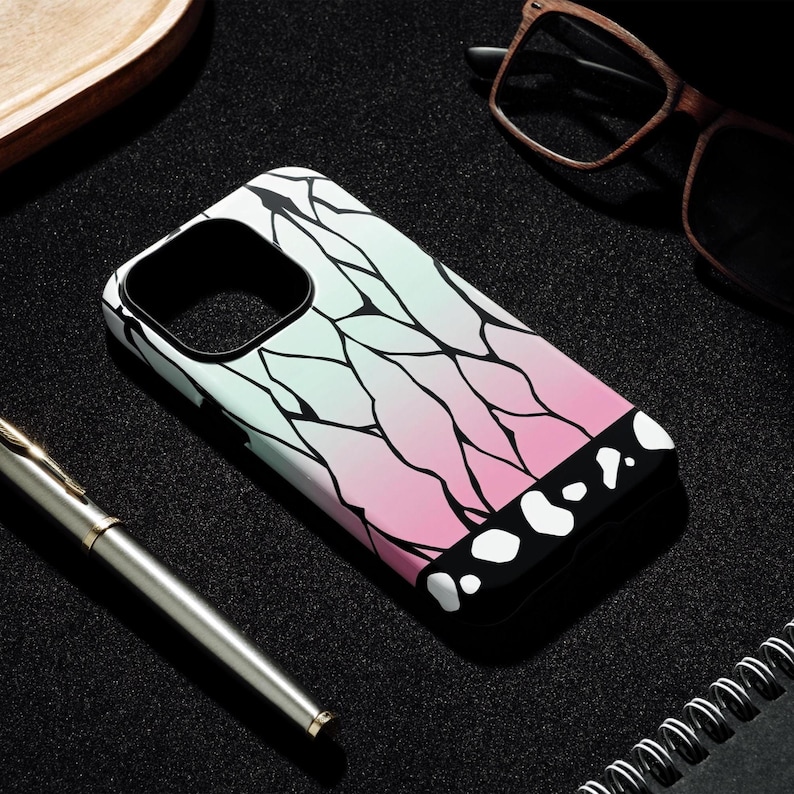 May include: A phone case with a gradient design of light green to pink, featuring black vein-like patterns. The bottom edge is black with white circular shapes. The case is on a black surface with a pen and glasses.
