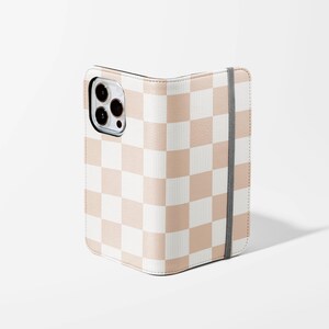 May include: A pink and white checkered phone case with a flap that folds over the screen. The case has a strap on the right side.