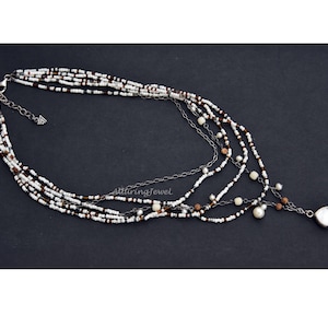 May include: Multi-strand necklace with white, brown, and black beads, a silver chain, and a large white pearl pendant.