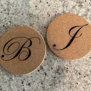 May include: Two cork coasters with the letters "B" and "J" in a cursive font.