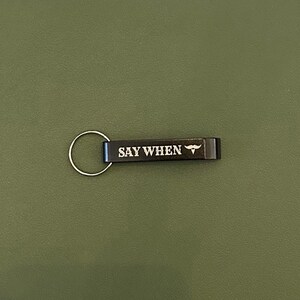 May include: Black metal bottle opener with a silver key ring. The opener has the text "SAY WHEN" and a small mustache graphic.