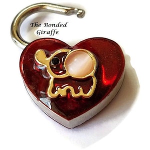 May include: Red heart-shaped padlock with a gold elephant design. The padlock has a silver shackle and the text "The Bonded Giraffe" is printed on the shackle.