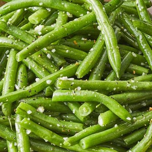 May include: A brown bowl filled with bright green, cooked green beans. The beans are seasoned with salt and pepper, and appear to be lightly oiled. A simple, yet appetizing, side dish.