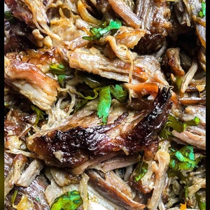 May include: Close-up of shredded, seasoned meat with a dark brown and light brown colour. The meat is topped with fresh green herbs.