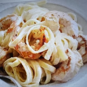Puede incluir: Un plato de fettuccine con camarones. La pasta está cubierta con una salsa cremosa blanca, y los camarones son de color naranja claro. Se ve un tenedor en la esquina inferior izquierda.