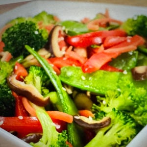 Puede incluir: Una ensalada colorida en un cuenco cuadrado blanco. La ensalada contiene floretes de brócoli, pimientos rojos en rodajas, guisantes verdes, zanahorias y setas shiitake. Semillas de sésamo espolvoreadas.