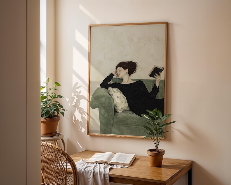 K&ouml;nnte beinhalten: Ein gerahmtes Gem&auml;lde einer Frau in einem schwarzen Kleid, die sich auf einem gr&uuml;nen Sofa zur&uuml;cklehnt und ein Buch liest. Das Gem&auml;lde ist vor einer hellbeigen Wand platziert, die von nat&uuml;rlichem Licht aus einem Fenster beleuchtet wird.