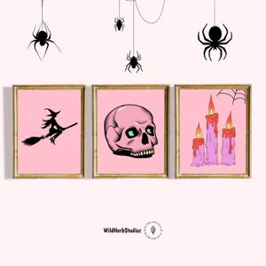 Puede incluir: Tres impresiones enmarcadas de color rosa con ilustraciones de tem&aacute;tica de Halloween. La primera impresi&oacute;n presenta una silueta negra de una bruja volando en una escoba. La segunda impresi&oacute;n presenta una calavera rosa con ojos verdes. La tercera impresi&oacute;n presenta tres velas rosas con llamas rojas.