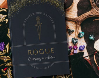 Puede incluir: Un cuaderno azul oscuro con detalles de purpurina dorada y un contorno dorado de una daga. El cuaderno dice "Rogue Campaign Notes" en la portada.
