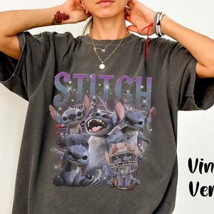K&ouml;nnte beinhalten: Dunkelgraues T-Shirt mit einem Aufdruck der Figur Stitch aus Lilo & Stitch, mit dem Wort "STITCH" &uuml;ber dem Bild. Das Design zeigt mehrere Stitch-Charaktere in verschiedenen Posen. Die Worte "Vintage Version" sind auf der rechten Seite aufgedruckt.
