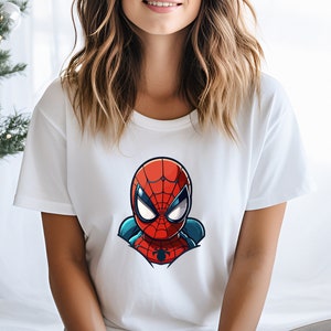 May include: White t-shirt featuring a cartoon illustration of Spider-Man's head. The design includes red, blue, and black colors. The shirt is a crew neck style.