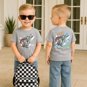 Puede incluir: Un ni&ntilde;o peque&ntilde;o con una camiseta gris con un dise&ntilde;o de Toy Story en la parte delantera y trasera. La parte delantera de la camiseta presenta a Woody y Buzz Lightyear. La parte trasera de la camiseta dice "To Infinity and Beyond!". El ni&ntilde;o tambi&eacute;n lleva gafas de sol y una mochila a cuadros en blanco y negro.