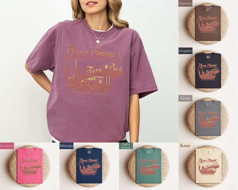 Puede incluir: Una camiseta de color malva con un gr&aacute;fico dorado de "Pizza Planet" de estilo vintage. La imagen muestra la camiseta en una persona y tambi&eacute;n muestra la camiseta en varios colores, incluyendo espresso, grafito, gris e marfil.