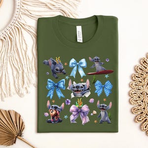 Puede incluir: Una camiseta verde oliva con un gr&aacute;fico colorido del personaje Stitch de Lilo & Stitch. El dise&ntilde;o incluye a Stitch en varias poses, rodeado de lazos azules y morados, conchas marinas y estrellas de mar. La camiseta tiene cuello redondo y una etiqueta.