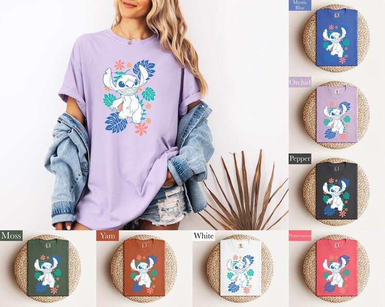 Puede incluir: Una camiseta de color lila claro con un personaje de dibujos animados y un dise&ntilde;o floral. La camiseta la lleva una persona, con otras camisetas en azul, morado, negro, verde, naranja, blanco y rojo, cada una con el mismo dise&ntilde;o.