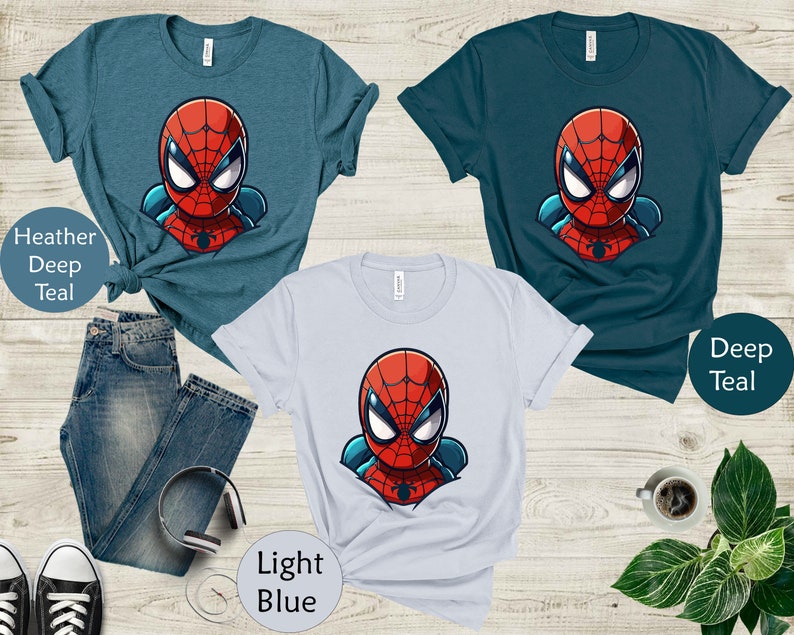 May include: Three t-shirts in teal and light blue with a cartoon Spider-Man graphic. The shirts are displayed with a pair of blue jeans, black and white sneakers, and headphones. The text on the image reads "Heather Deep Teal", "Deep Teal", and "Light Blue".